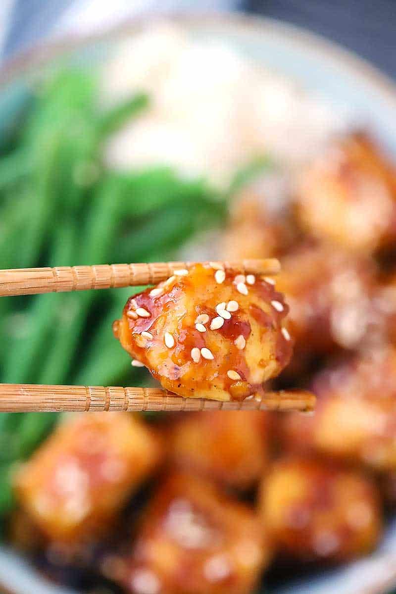 Chopsticks holding a piece of sesame chicken.