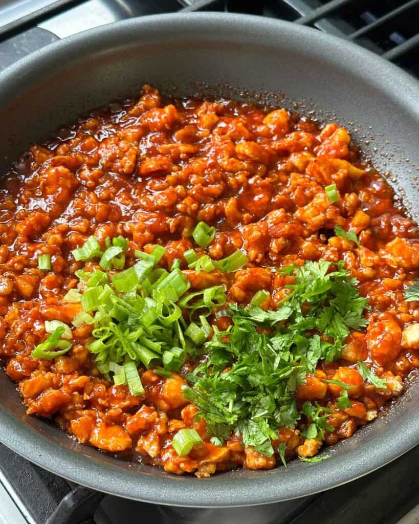 Gochujang tofu in a skillet with cilantro and green onions added in.