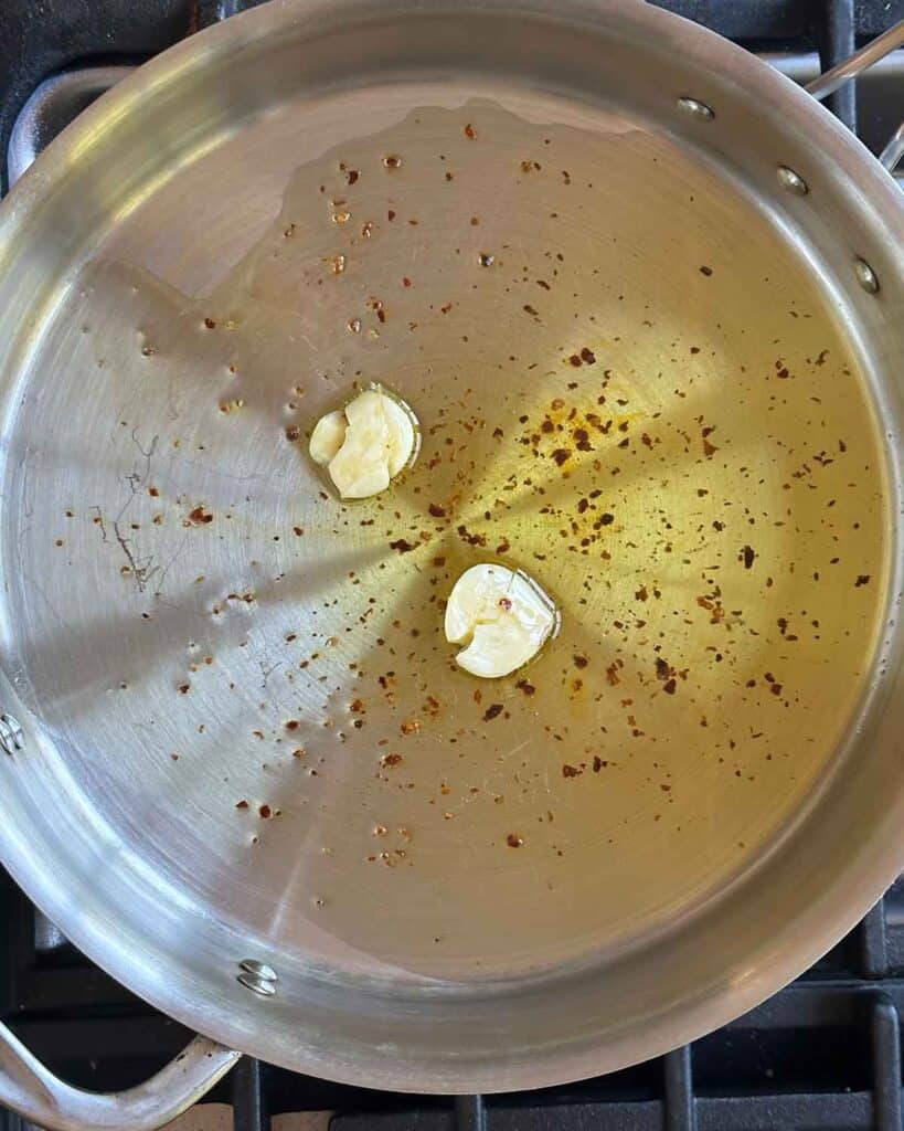 A skillet with olive oil, garlic cloves, and crushed red pepper.
