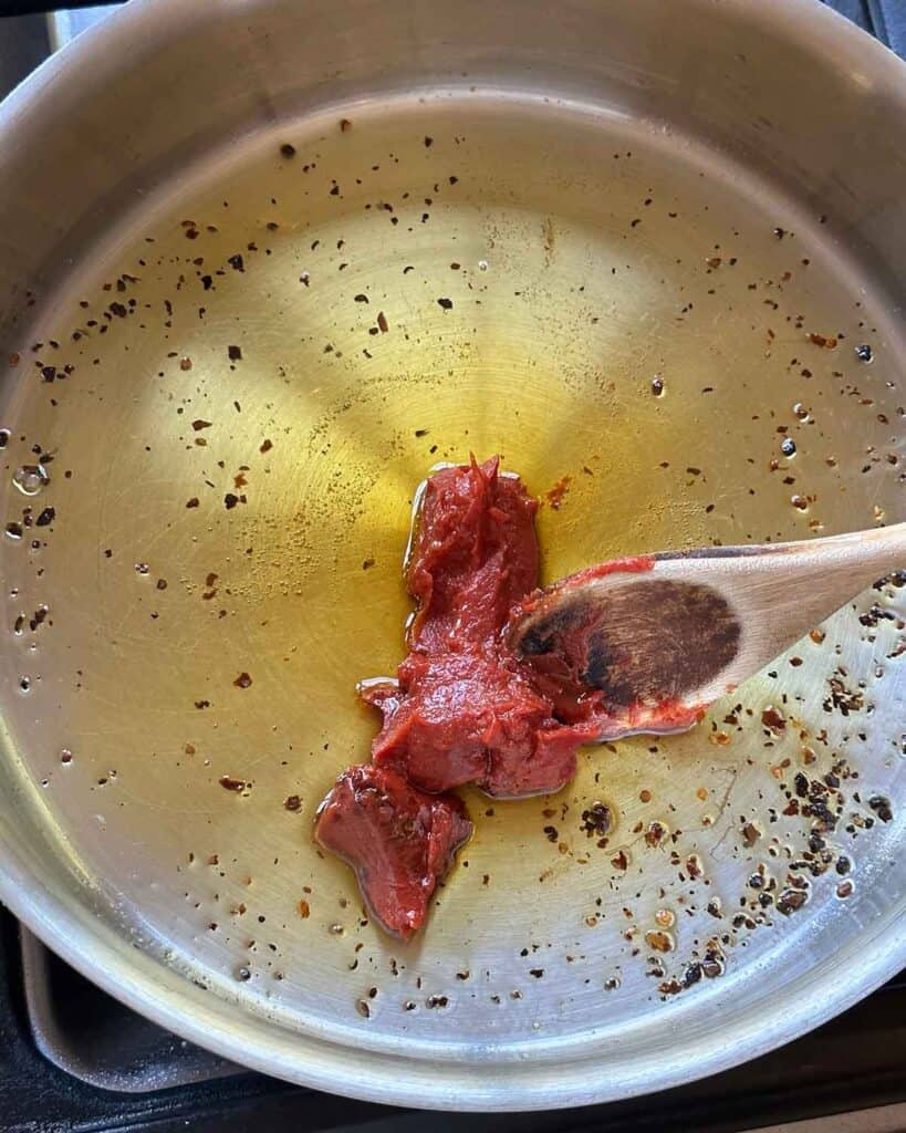 Stirring tomato paste into oil in a skillet.