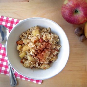 Oatmeal in white bowl on wooden table with red checkered napkin.