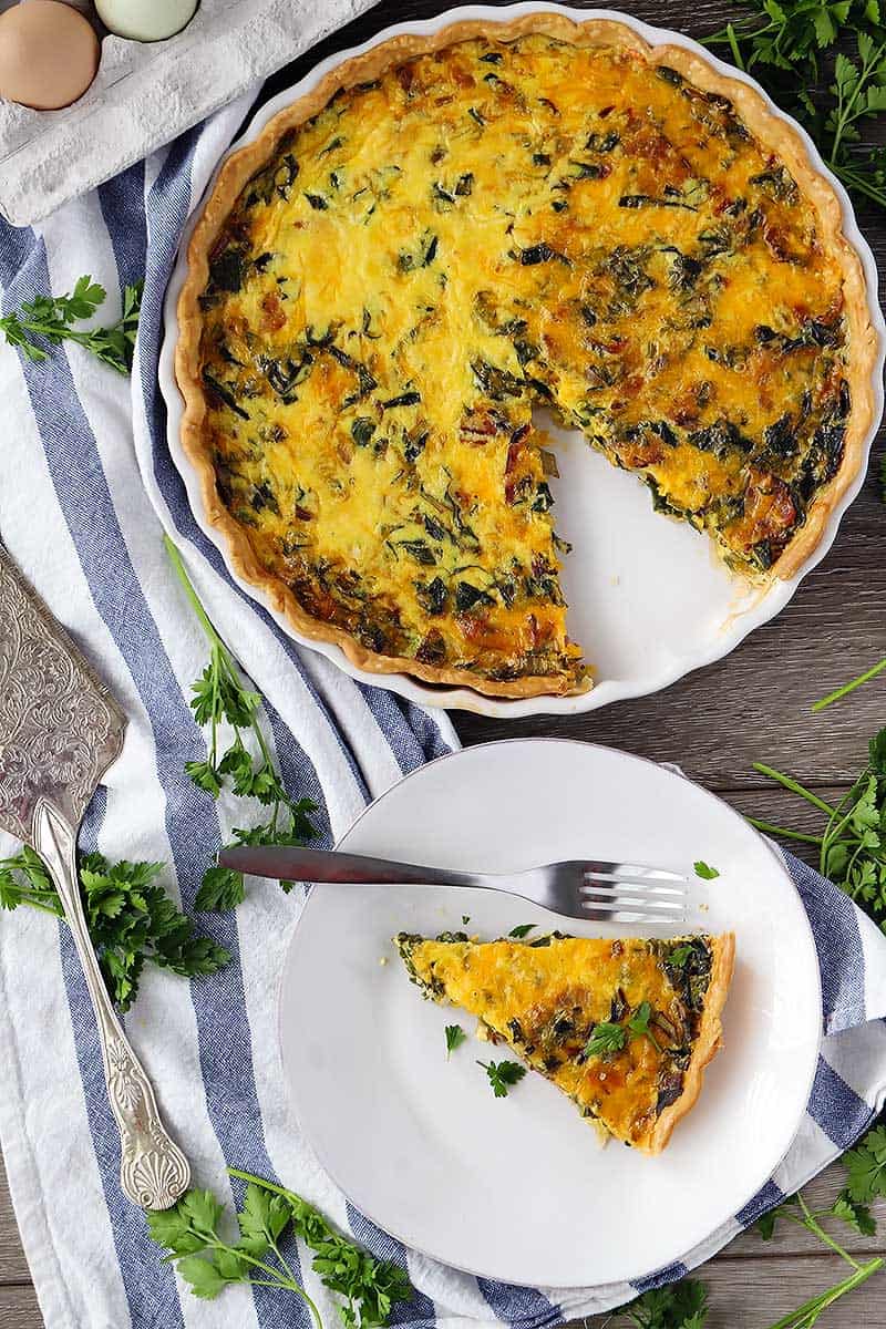 A slice of quiche on a plate taken out of the whole thing.