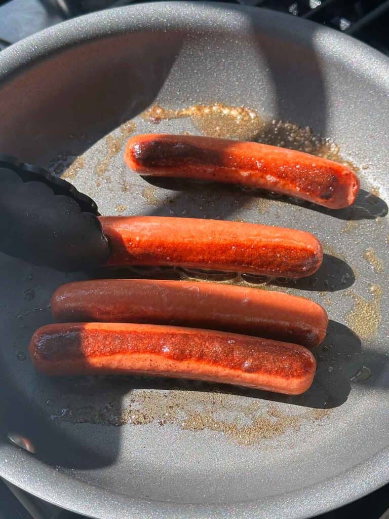 Hot dogs cooking in butter in a skillet.