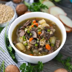 Square photo of a bowl of beef barley soup with mushrooms.