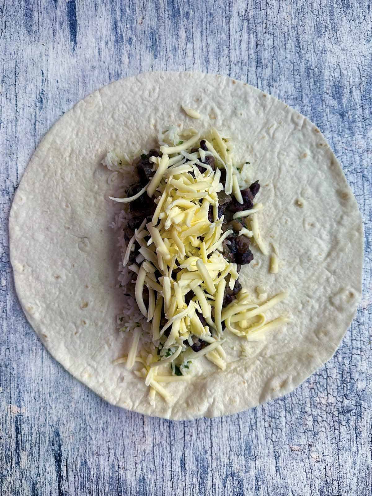 Open tortilla on with cheese, beans, and rice in center.