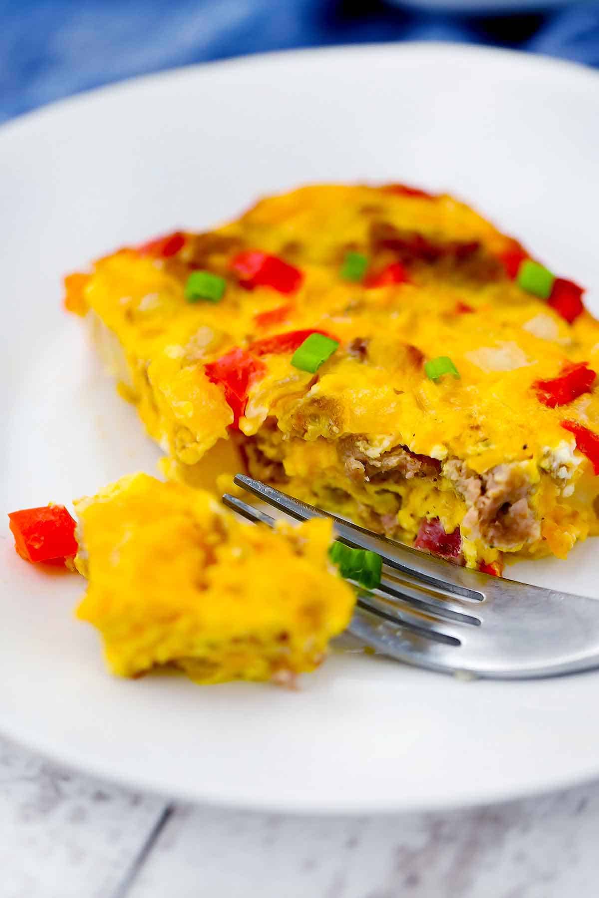 Close up photo of a slice of breakfast casserole with a fork taking a piece out of it.