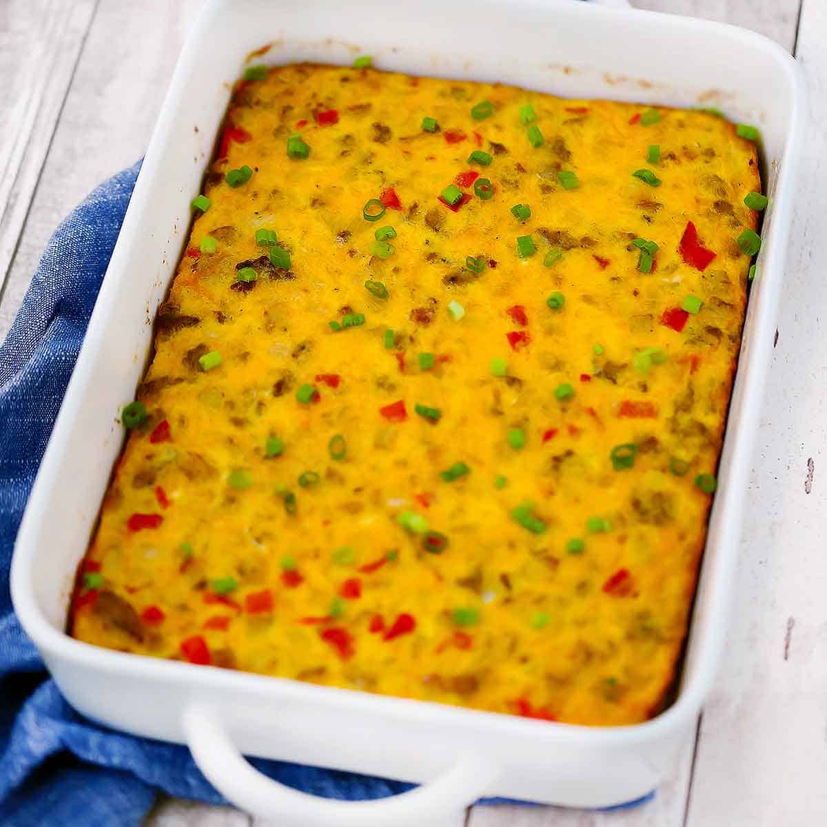 Square photo of a white baking dish with breakfast egg sausage casserole on a blue towel.