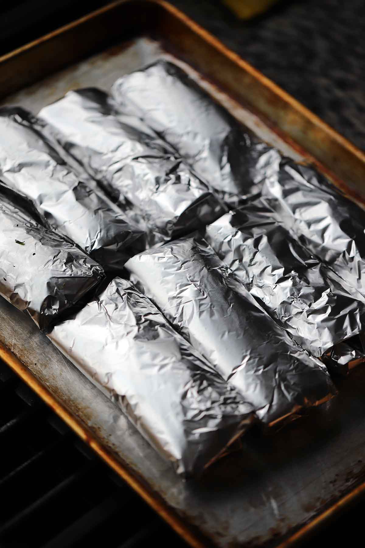 Breakfast tacos wrapped in foil on a rimmed baking sheet.