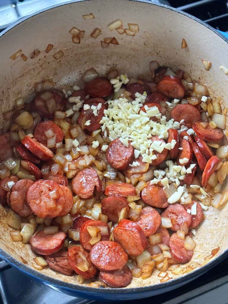 Adding garlic to linguiça and onions sautéing in a dutch oven.