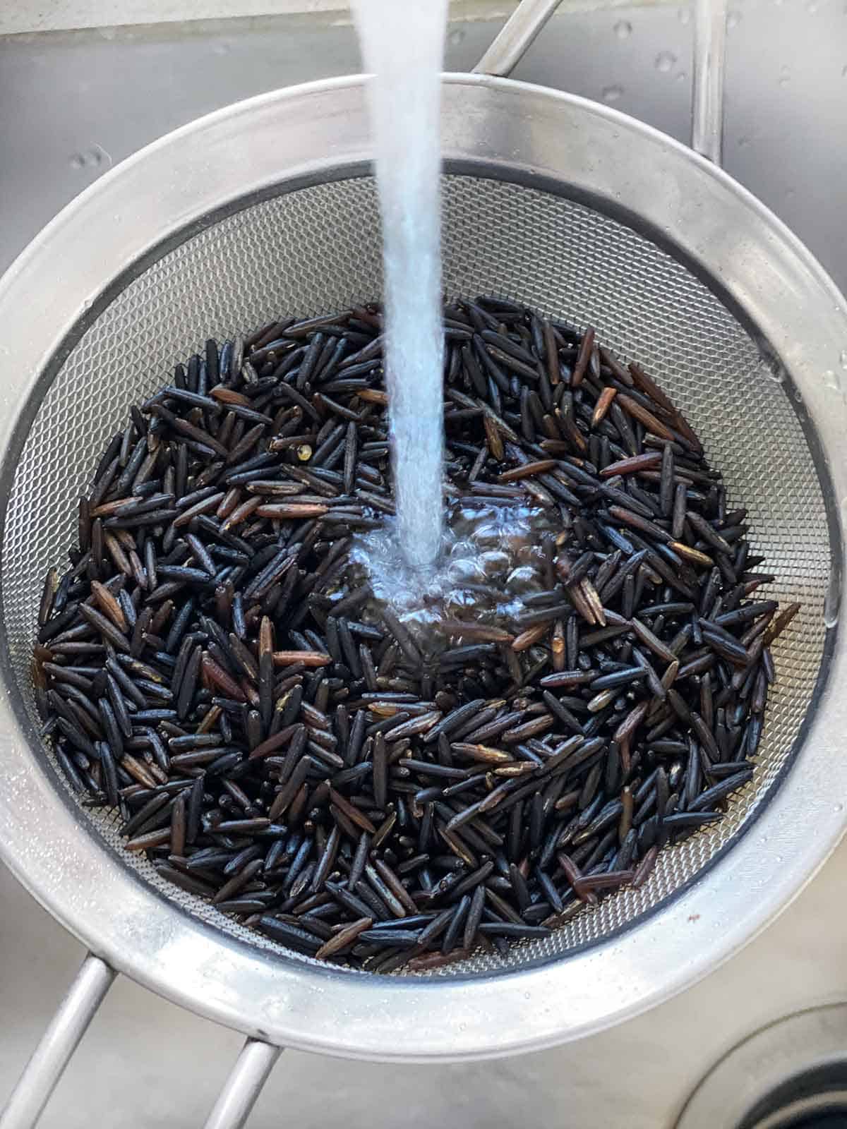 Rinsing wild rice off in a mesh sieve in a sink.