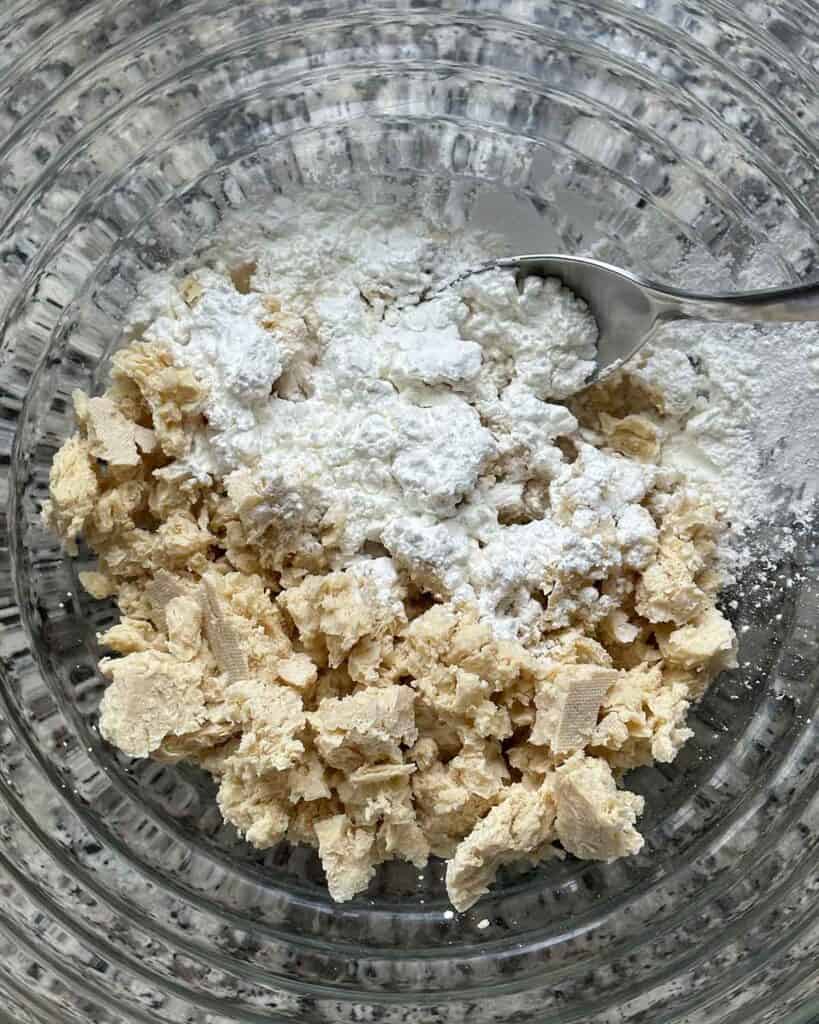 Coating torn tofu with cornstarch in a bowl.