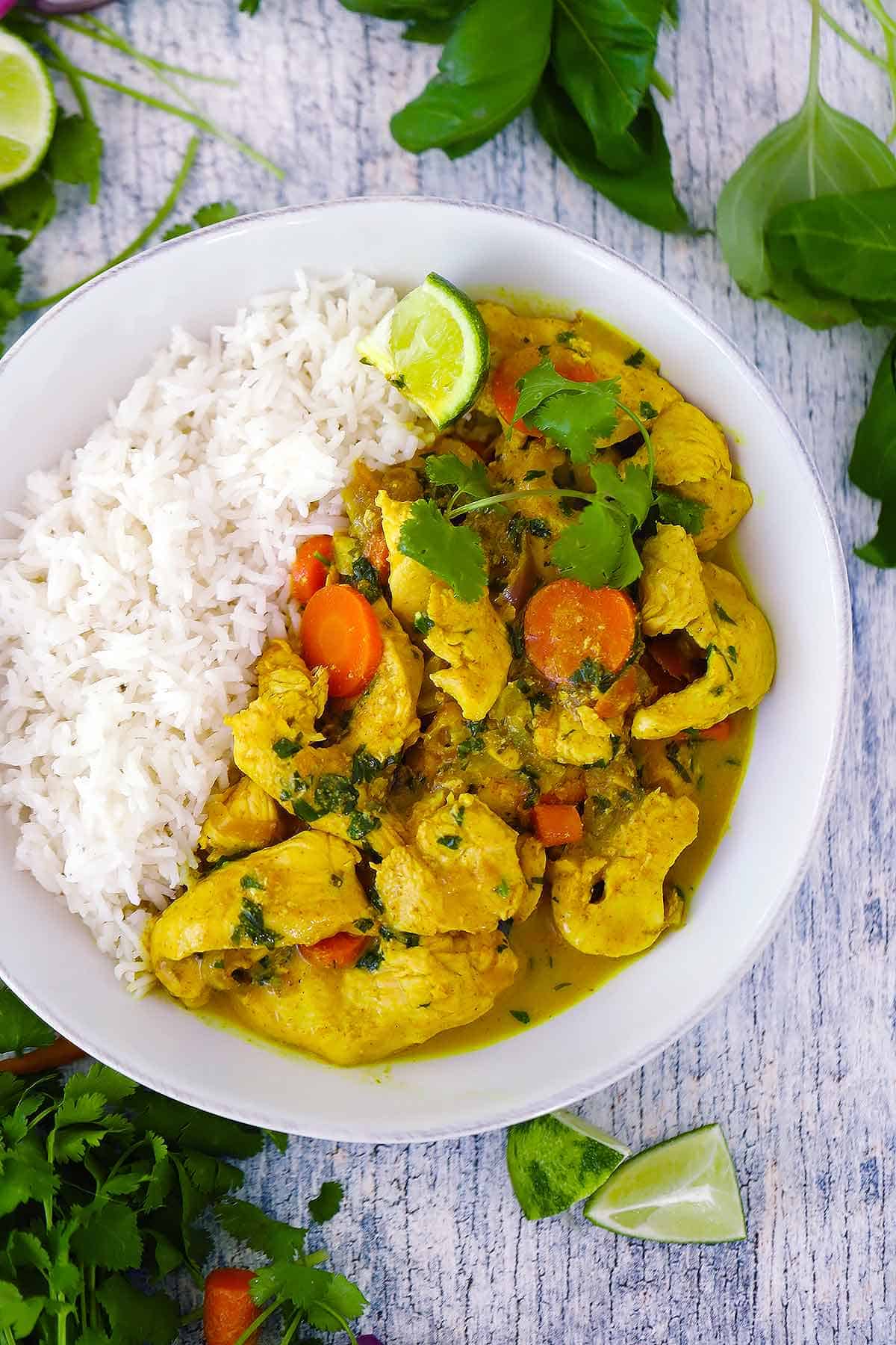 Overhead photo of a bowl of coconut chicken curry with basmati rice, a lime wedge, and cilantro sprigs.