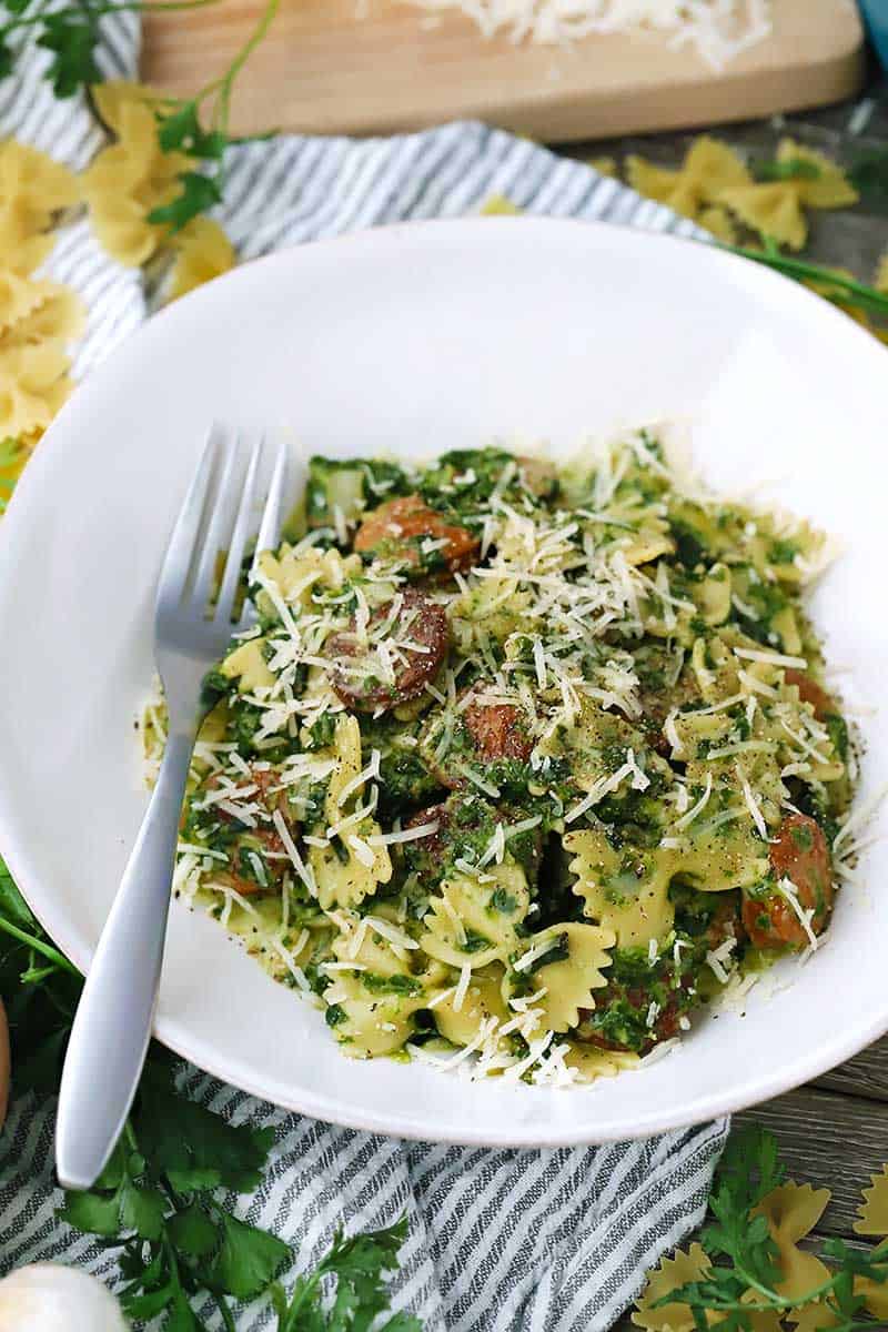 A white bowl of pasta with sausage and spinach.