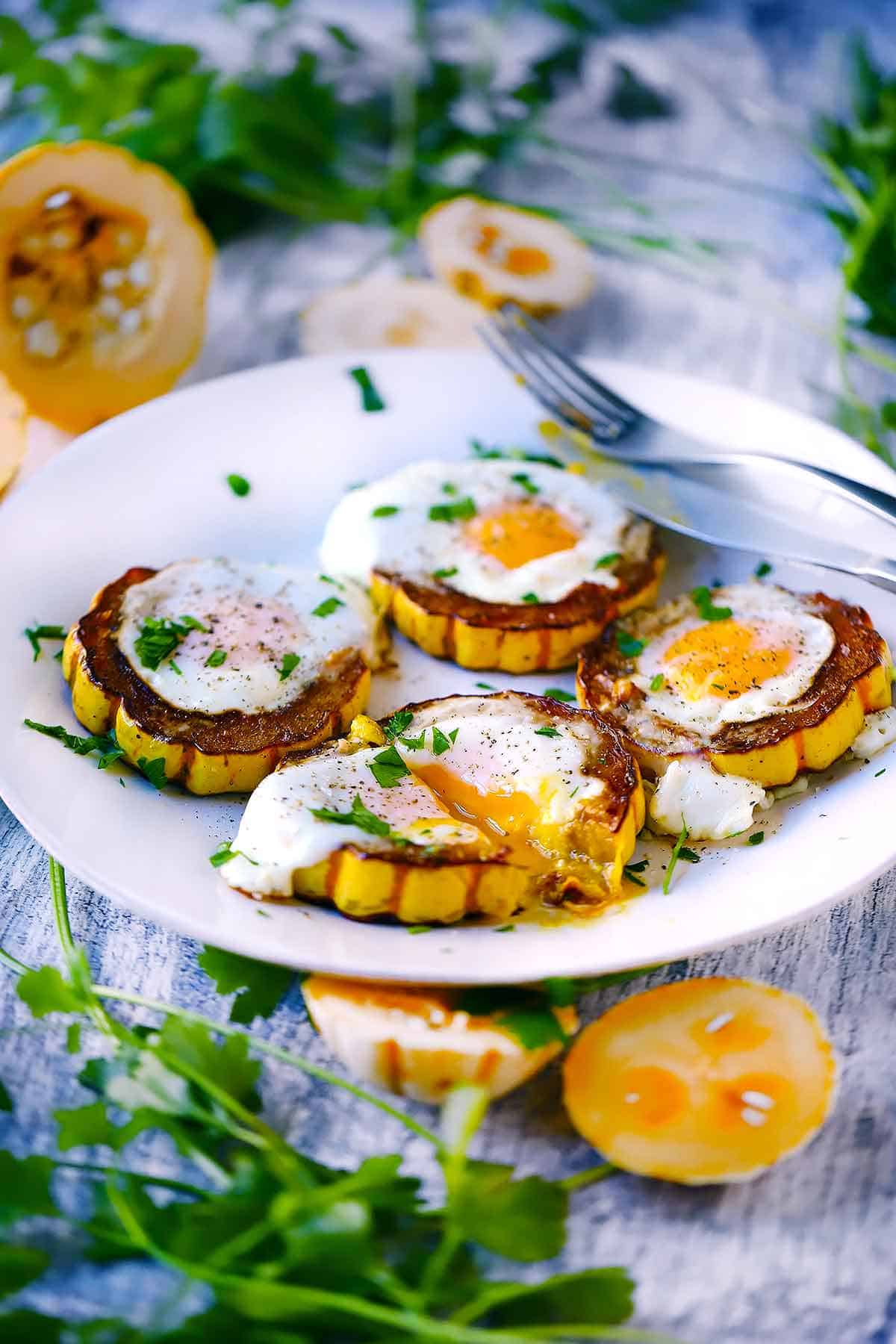 A white plate with delicata squash egg in a holes and herbs and squash in the background and foreground.