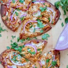 Bird's eye view of two BBQ Chicken Naan Pizzas on a wooden cutting board.