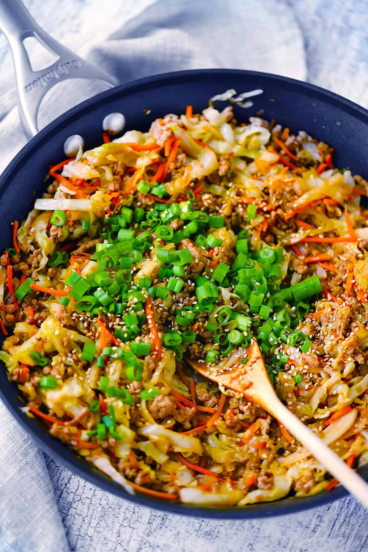 Egg roll in a bowl in a skillet - cabbage and carrots with ground pork and green onions, garlic, and ginger.