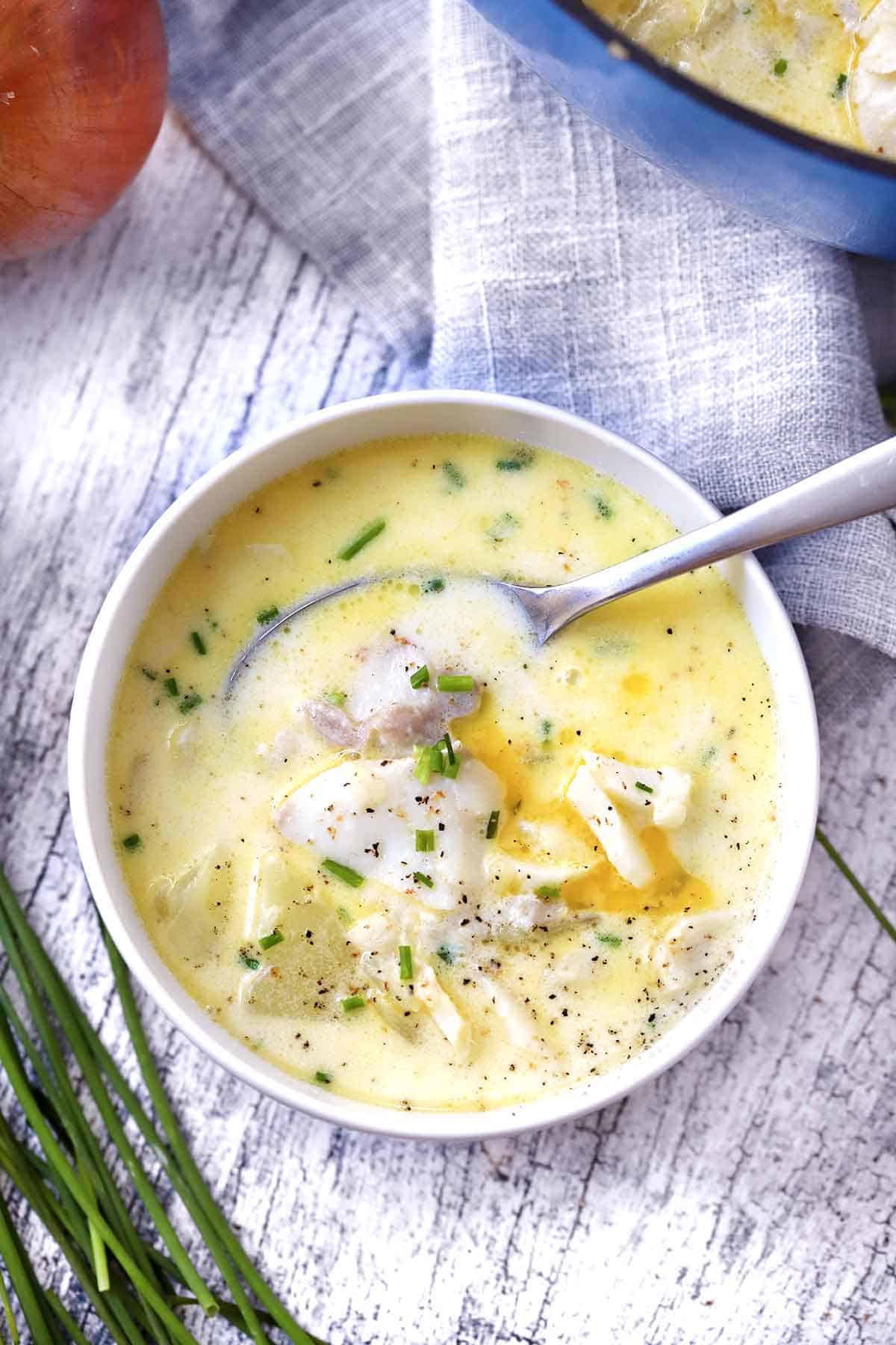 Overhead photo of a bowl of fish chowder with a spoon in it.