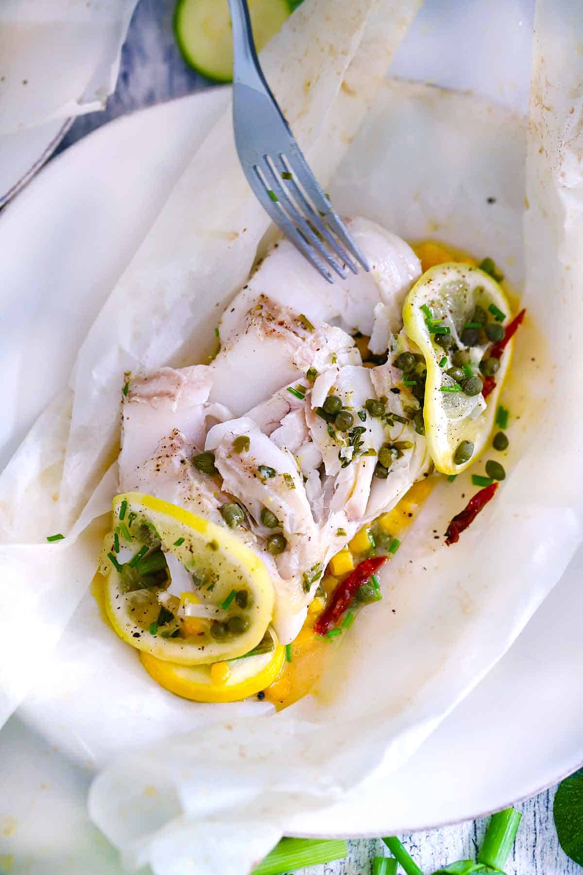 Cod in parchment paper, flaked apart with a fork showing texture of the fish.