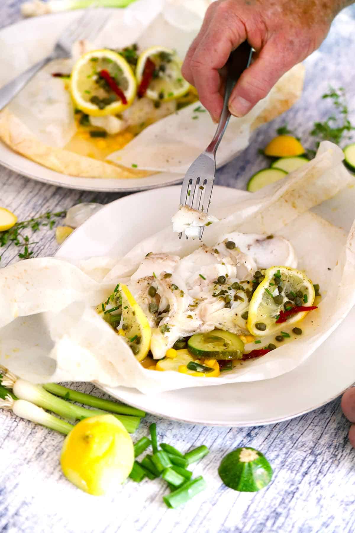 Image shows someone flaking apart cod in fish en papillote to show texture.