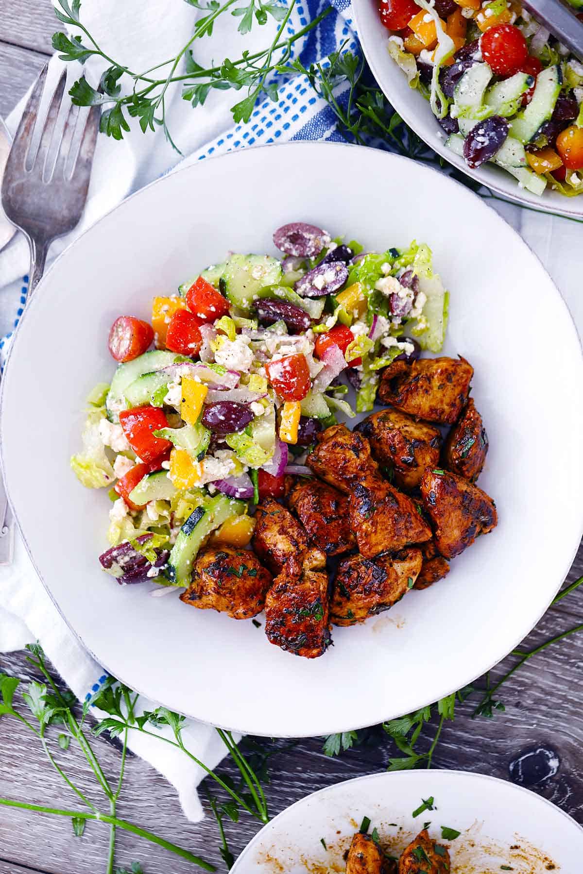 An overhead photo of Greek Chicken Bites and a Greek salad on a white plate.