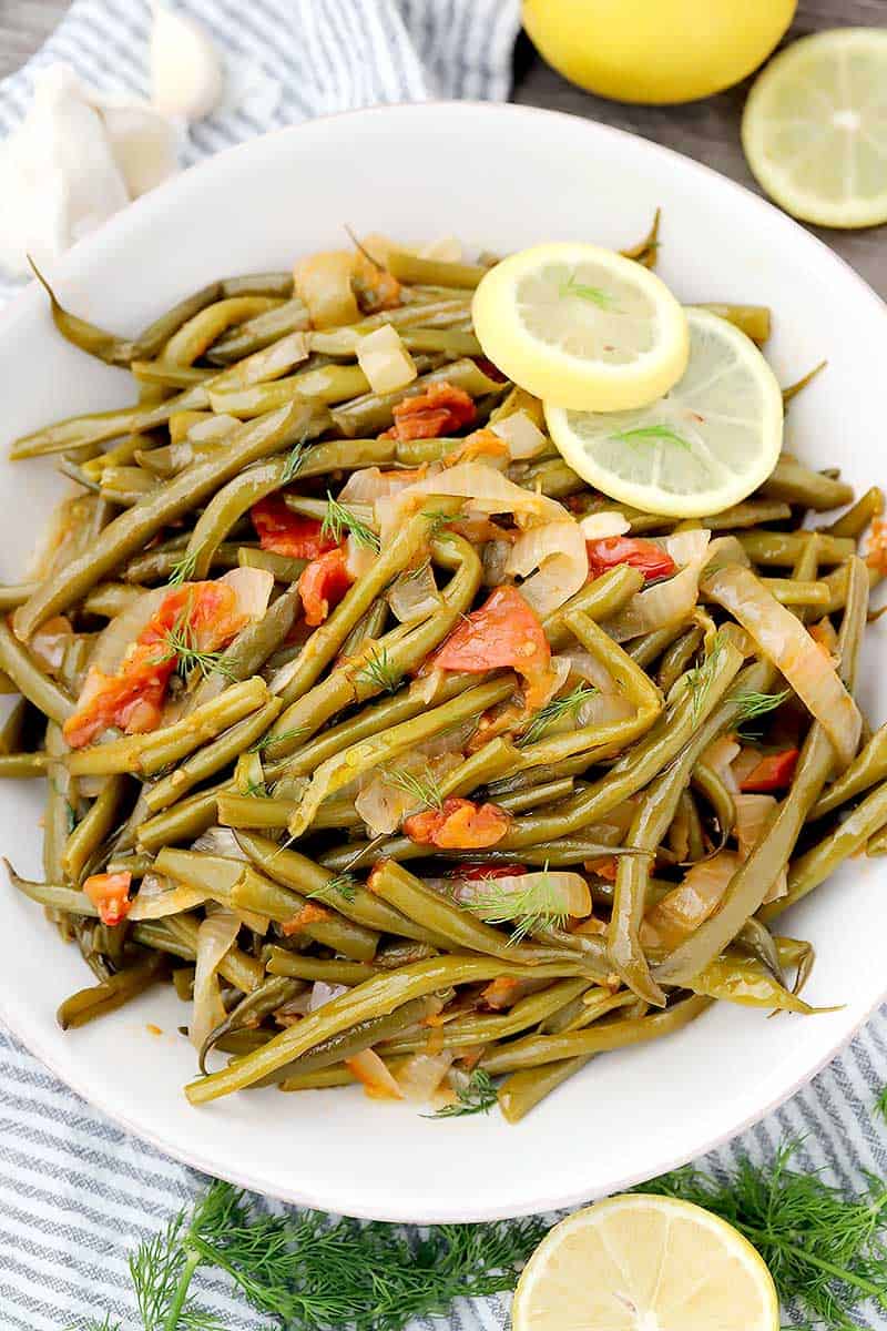 Overhead photo of Greek Green Beans with tomatoes and lemon in a white bowl.