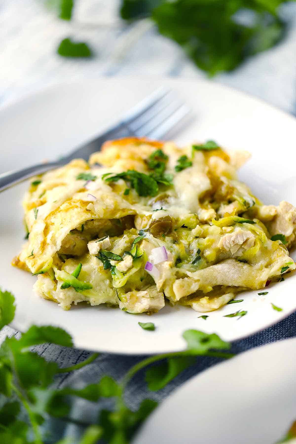 Close up photo of green chicken enchilada casserole on a white plate.