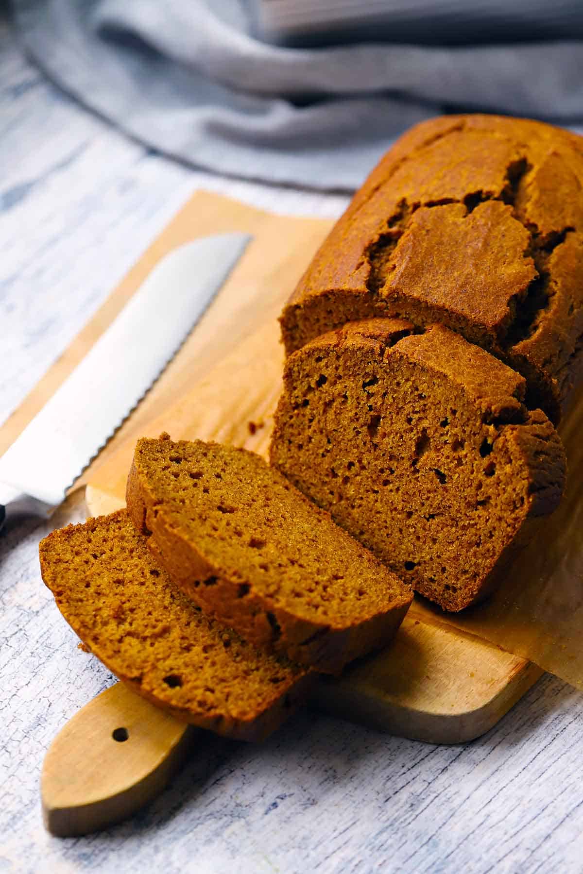 A loaf of healthy pumpkin bread made with whole wheat flour, maple syrup, and extra virgin olive oil on a wooden cutting board sliced into three pieces.