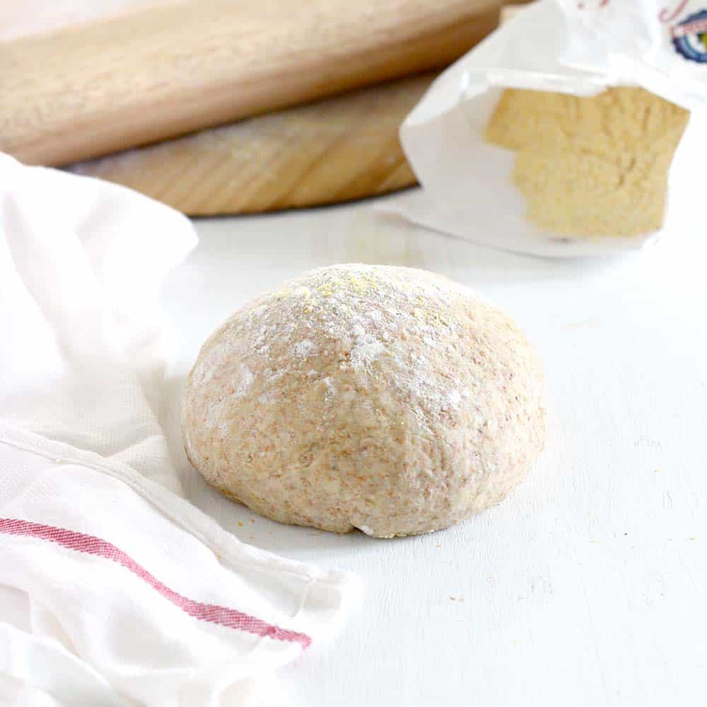 Ball of whole wheat pizza dough on a white surface.