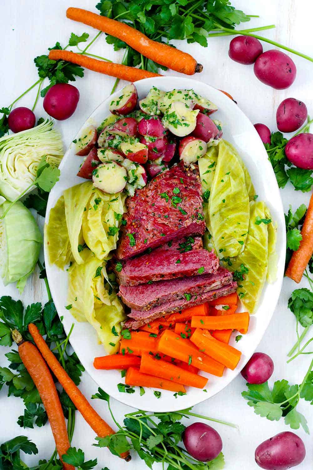 Overhead photo of Instant Pot corned beef and cabbage with carrots and buttered potatoes and ingredients scattered around.