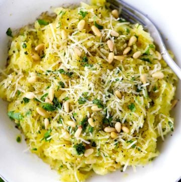 An overhead photo of a bowl of spaghetti squash with garlic, herbs, pine nuts, and parmesan cheese.