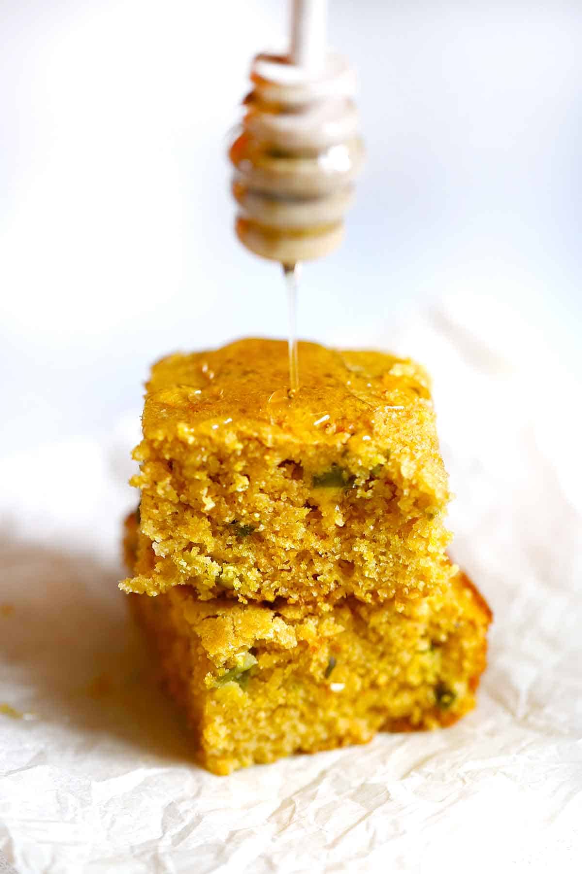 Two stacked pieces of jalapeño cornbread being drizzled with honey.