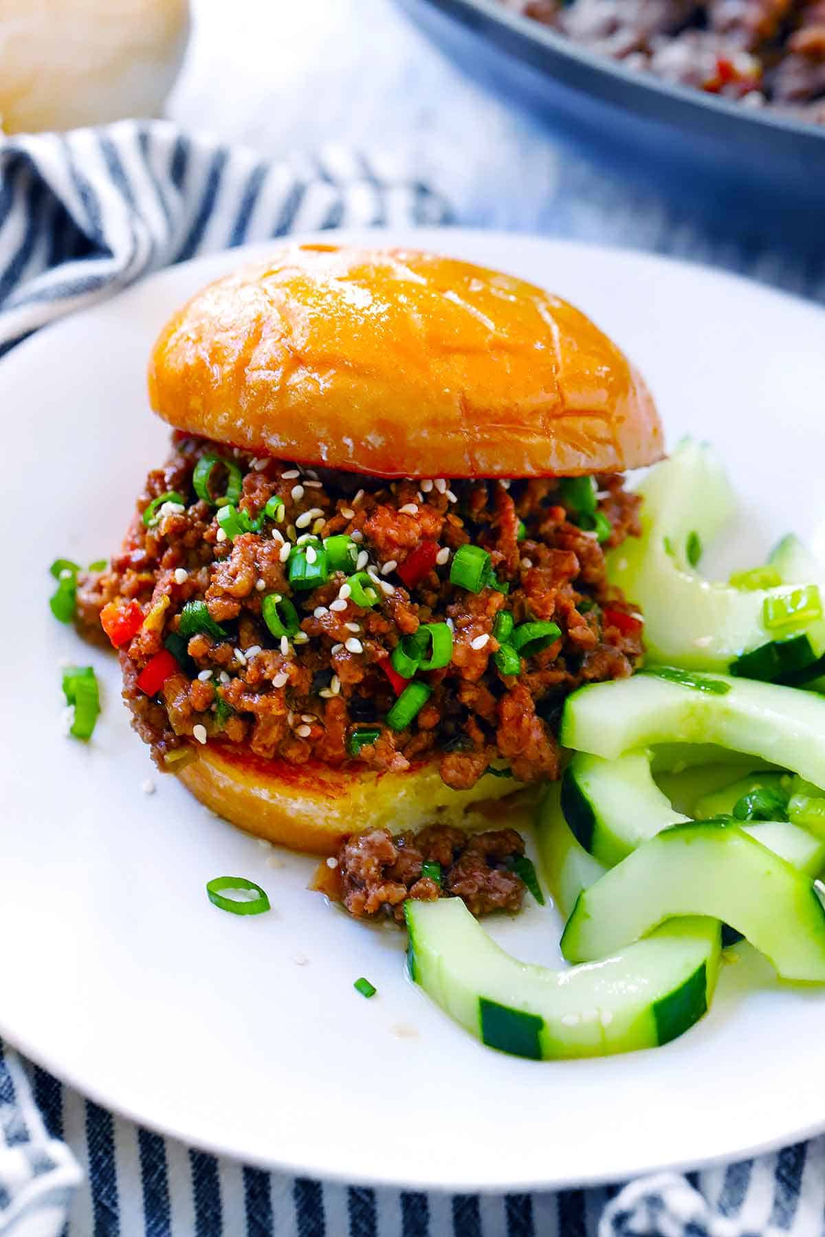 A sloppy joe on a white plate with Korean bbq sauce, green onions, and sesame seeds.