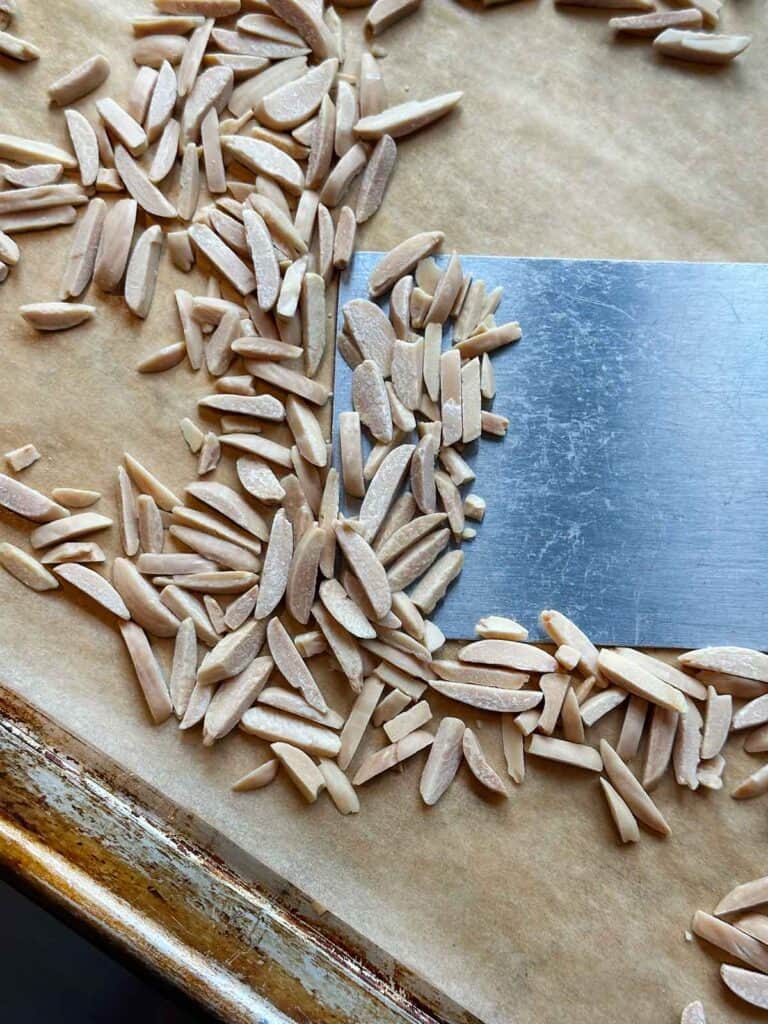 Toasted slivered almonds on a parchment covered baking sheet.