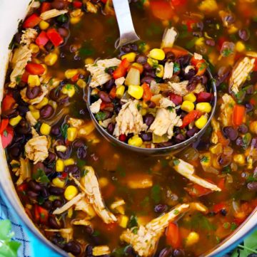 A ladle in a dutch oven with leftover turkey soup with black beans and corn in it.