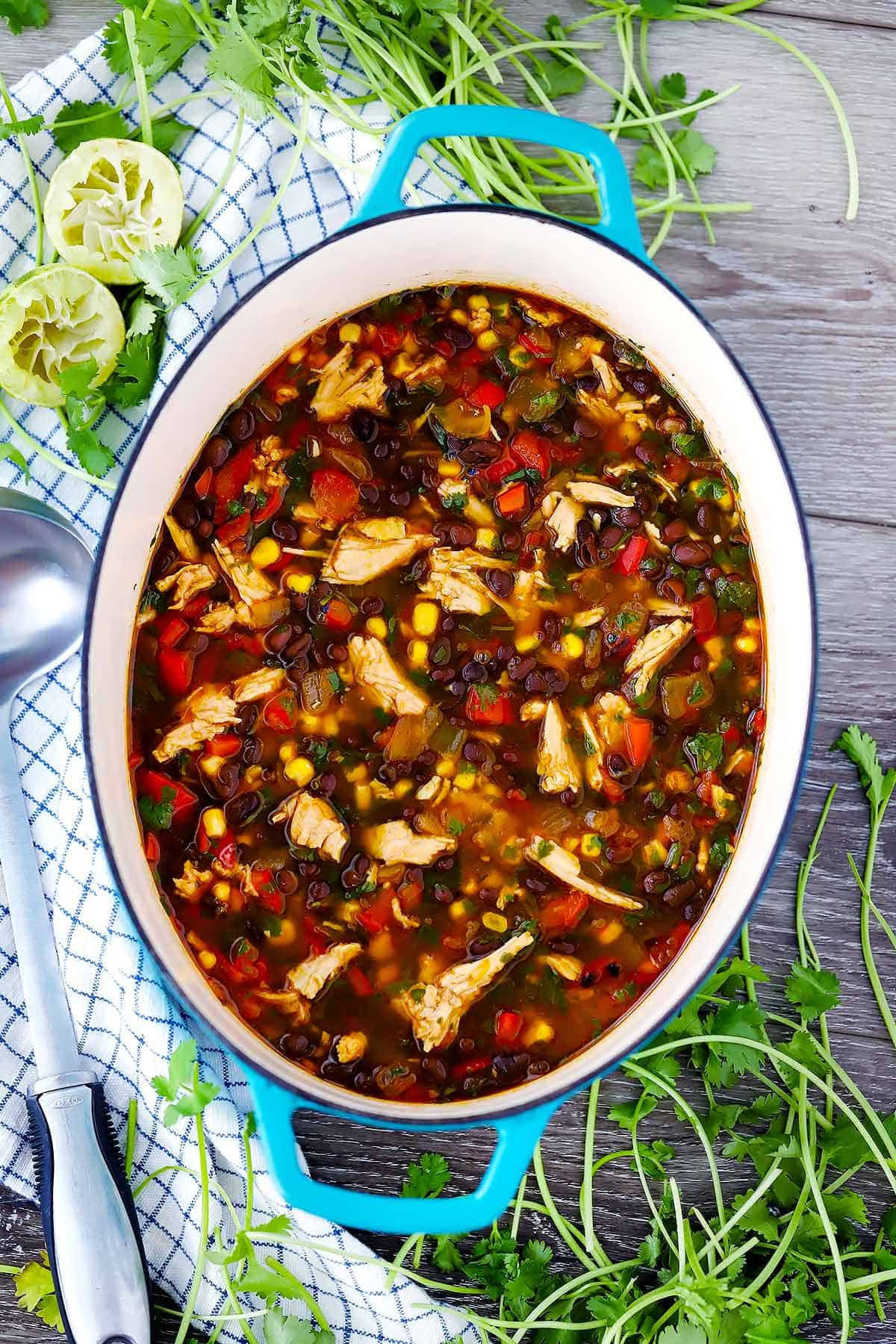 A dutch oven with leftover turkey soup and cilantro and limes in the background.
