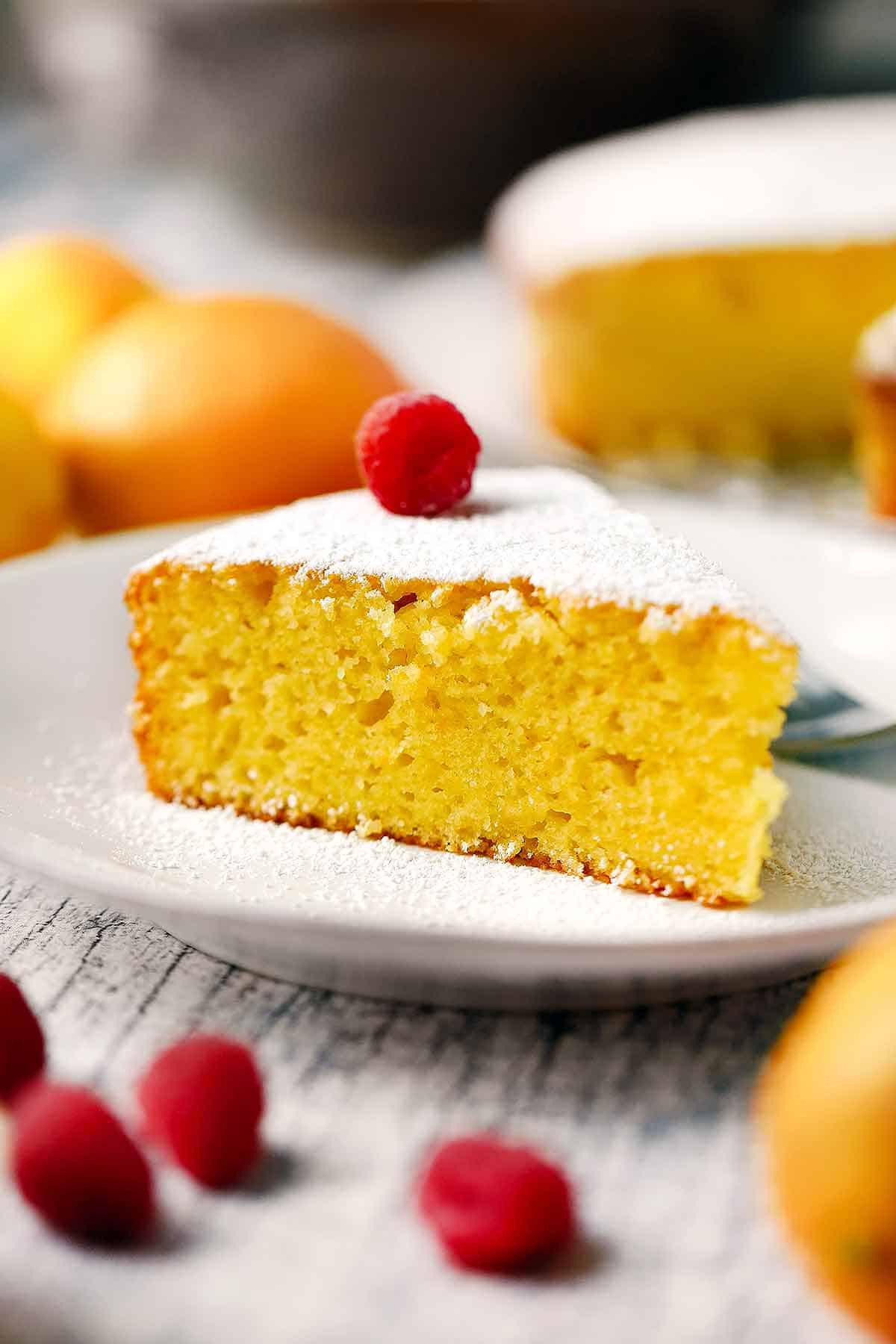 A slice of lemon olive oil cake with a raspberry on top on a white plate.