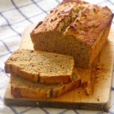 Loaf of poppy seed bread with two slices cut off, on wooden cutting board.