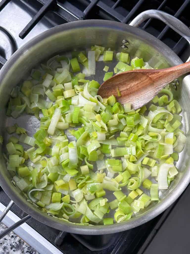 Sautéing leeks in olive oil in a deep skillet with a wooden spoon.