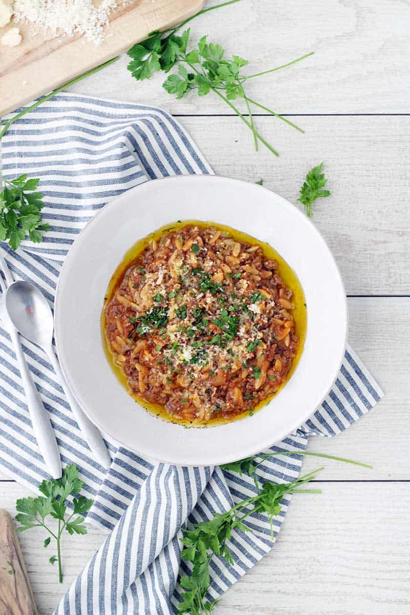 Bird's eye view of manestra in white bowl, on blue and white striped towel, with herb garnish.