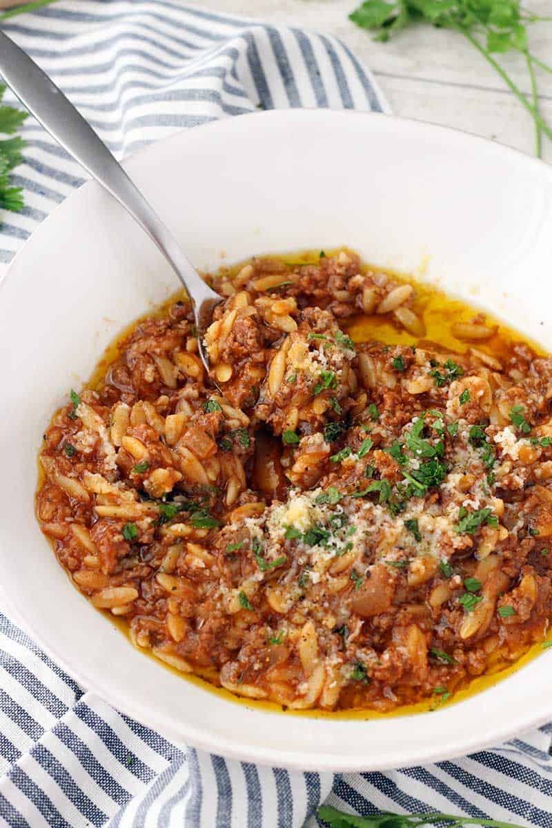 Close up bord's eye view of orzo and ground beef (manestra) in a white bowl, with spoon inside bowl.