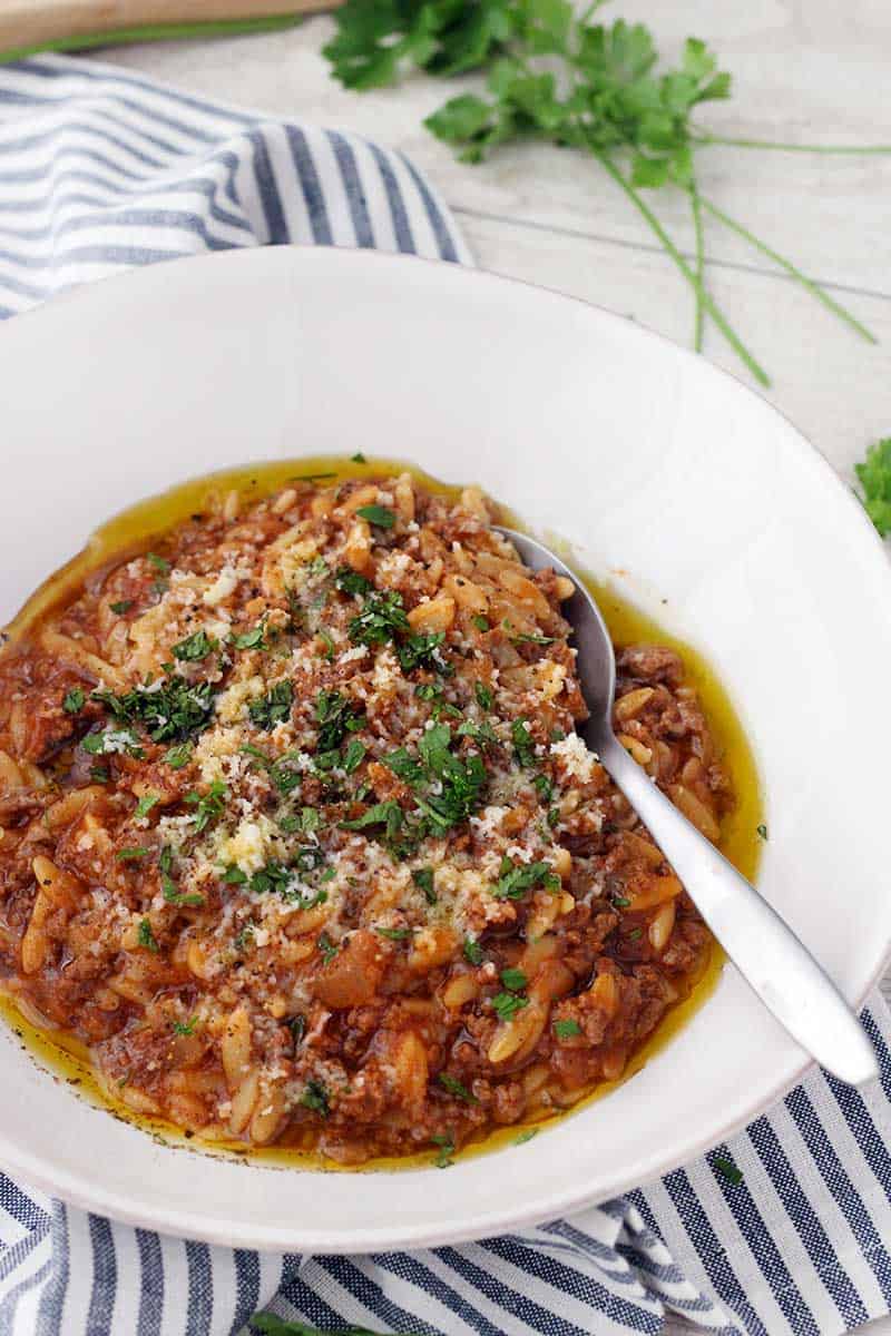 Close up bord's eye view of orzo and ground beef (manestra) in a white bowl, with spoon inside bowl.
