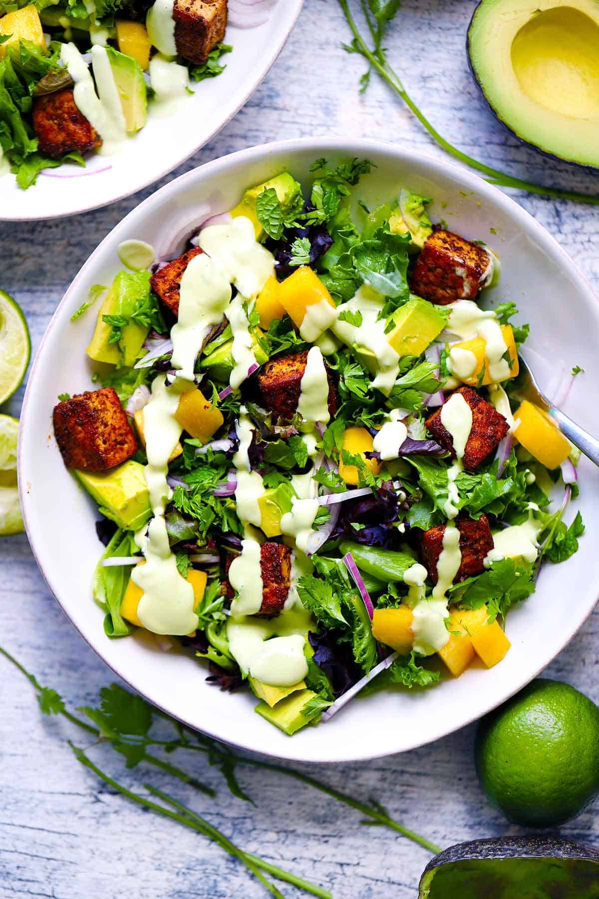 Overhead photo of a bowl of mango avocado salad with blackened tofu drizzles with avocado lime dressing.