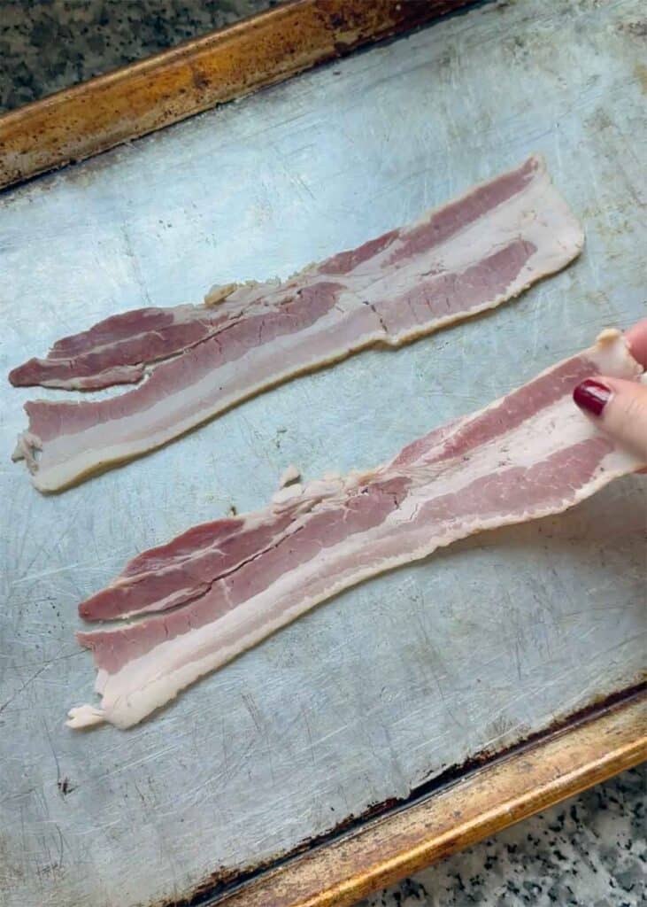 Two slices of bacon on a baking sheet before going in the oven.