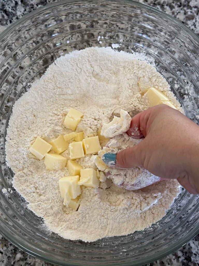 Showing how to incorporate cold cubed butter into flour mixture with hands to make base for scones.
