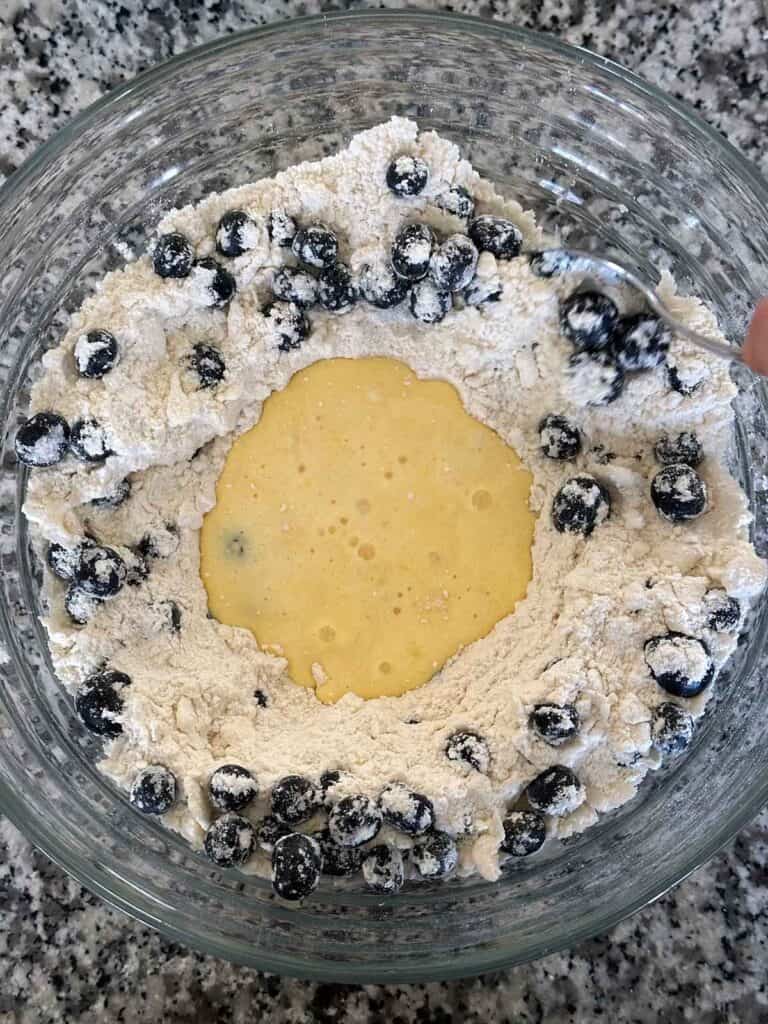 A well in the center of a flour blueberry mixture with egg and milk mixture poured in center.