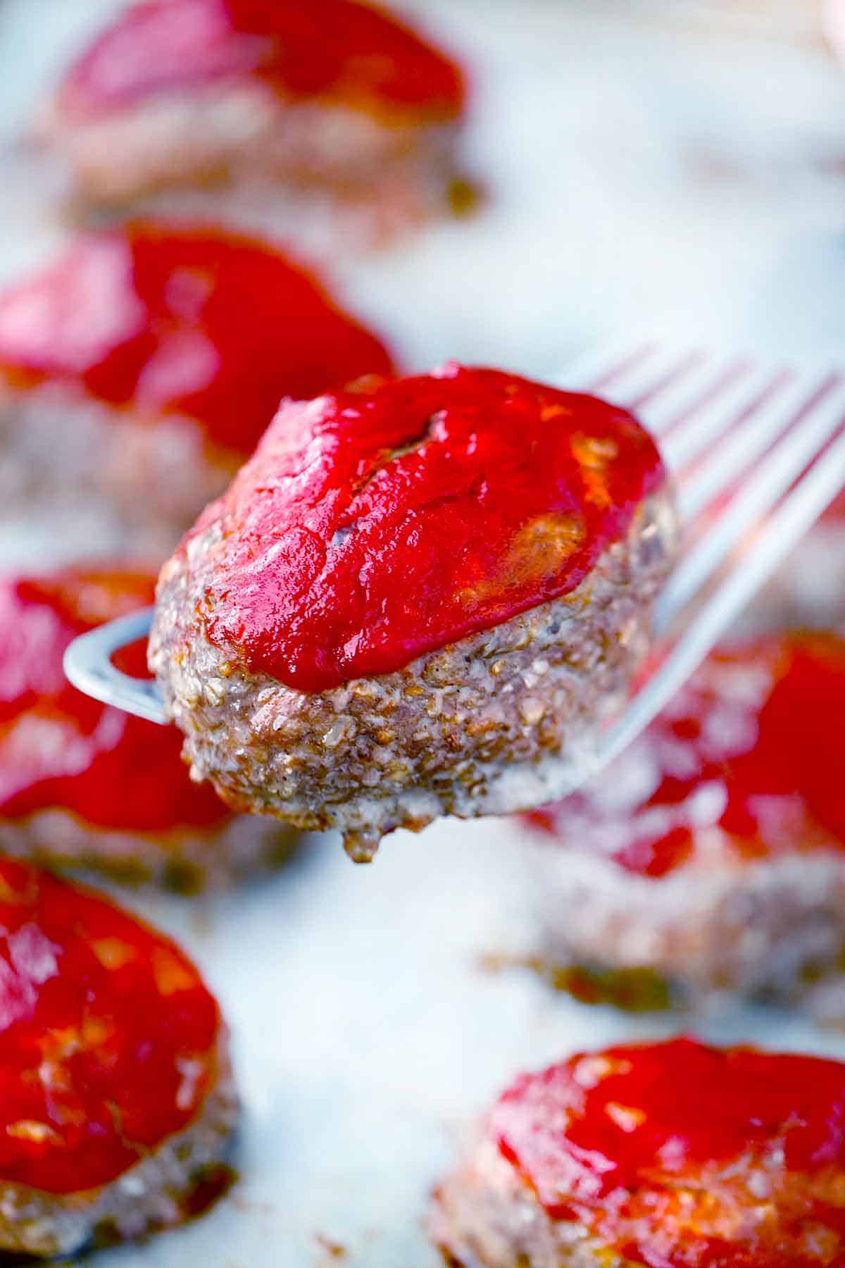 A spatula holding a mini meatloaf over a baking sheet.