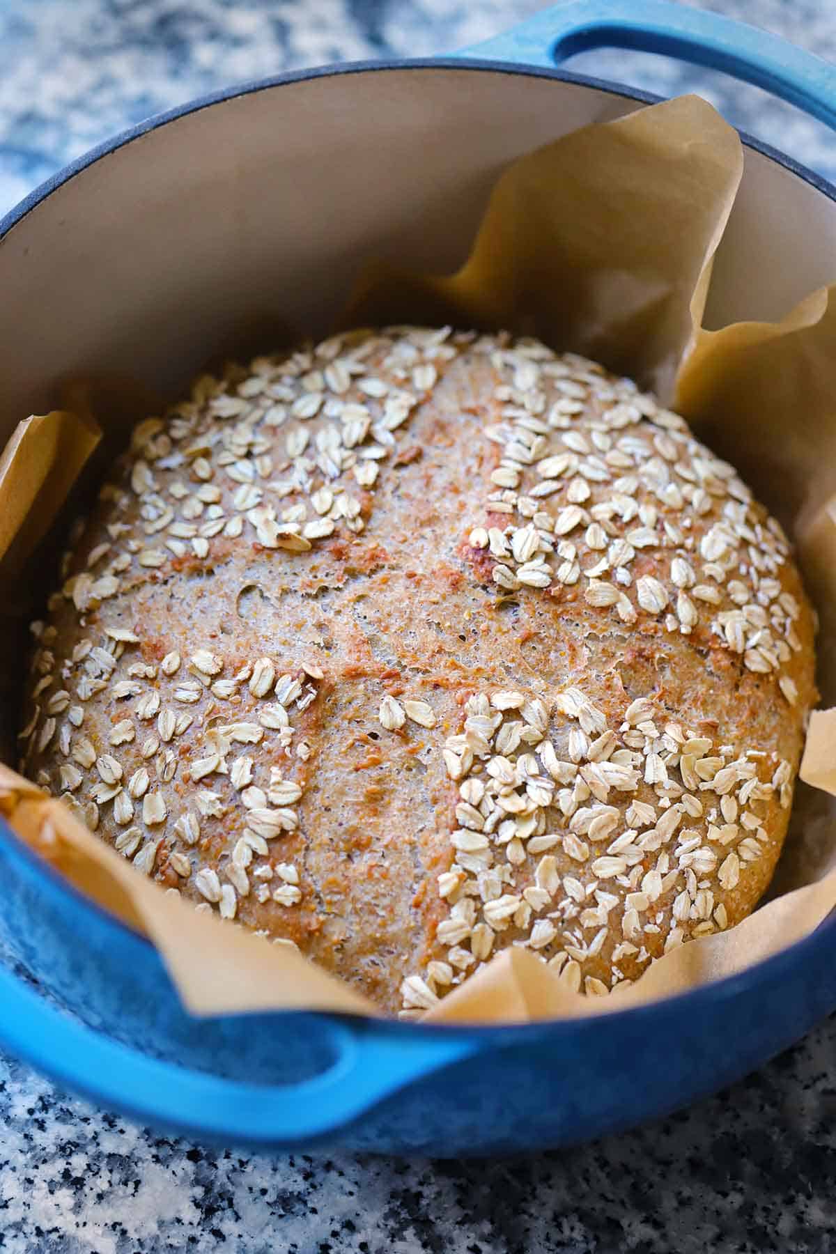Seeded multigrain no knead bread loaf after baking in a blue Dutch oven lined with parchment paper.