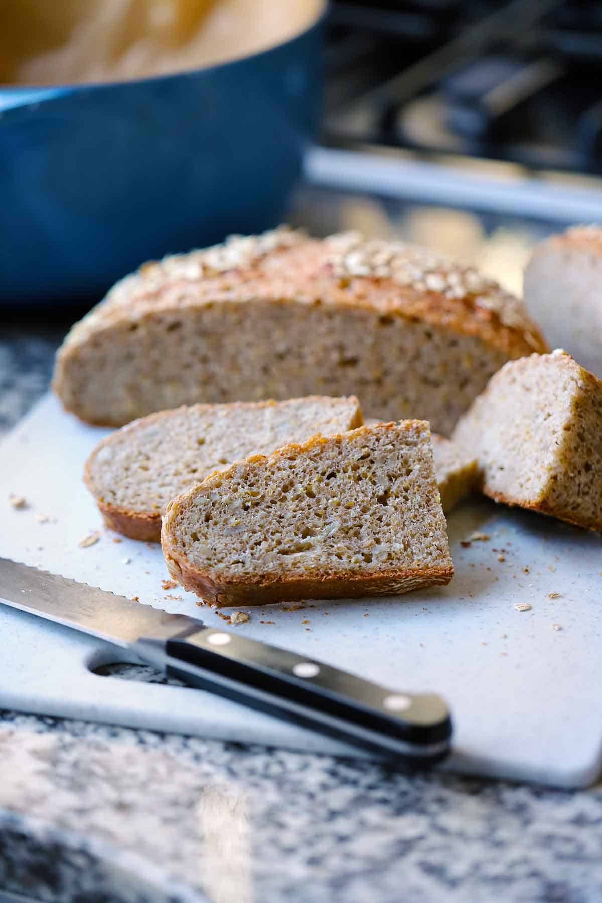 A seeded multigrain no knead bread sliced on a cutting board with a bread knife in the foreground.