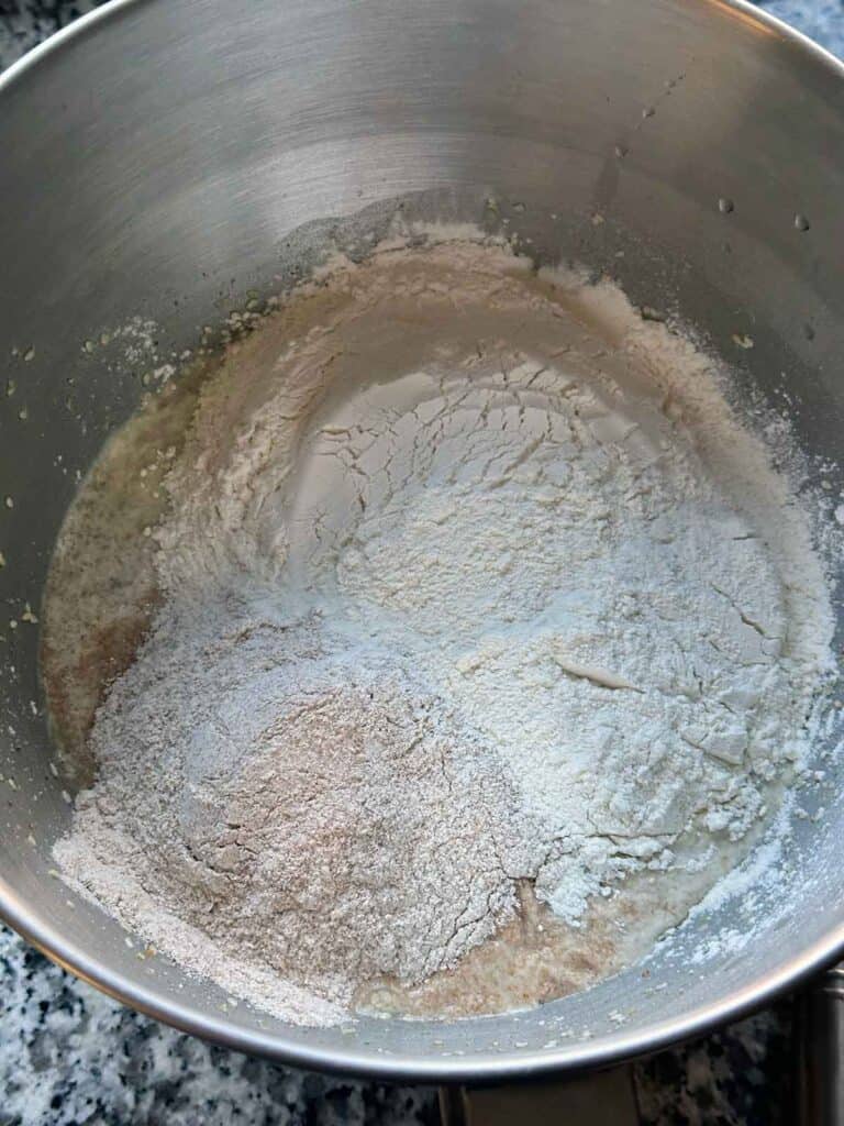 Adding bread flour and whole wheat flour to a no knead bread dough mix.