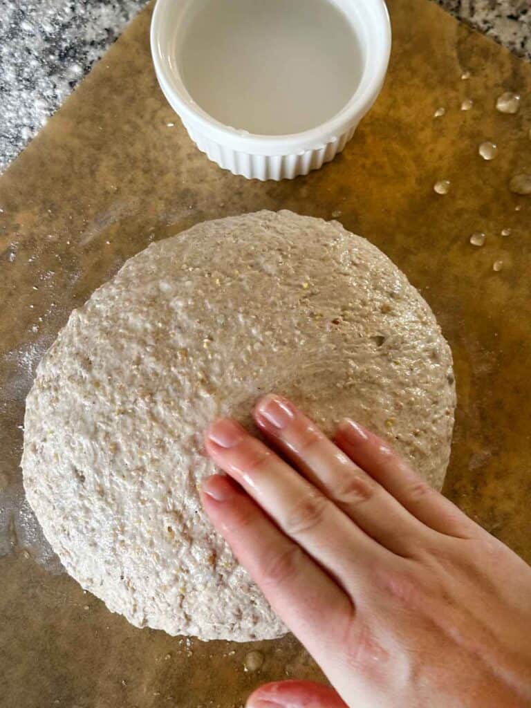 Getting the top of a loaf of bread wet in order to stick oats or seeds to.